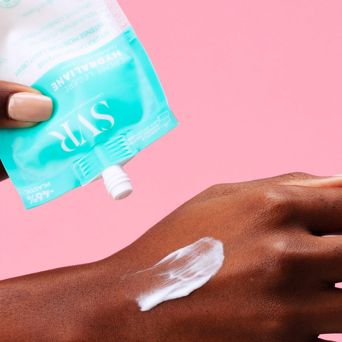 SVR Hydraliane Light Cream in a turquoise pouch being applied as a white lotion onto a person's hand against a pink background.