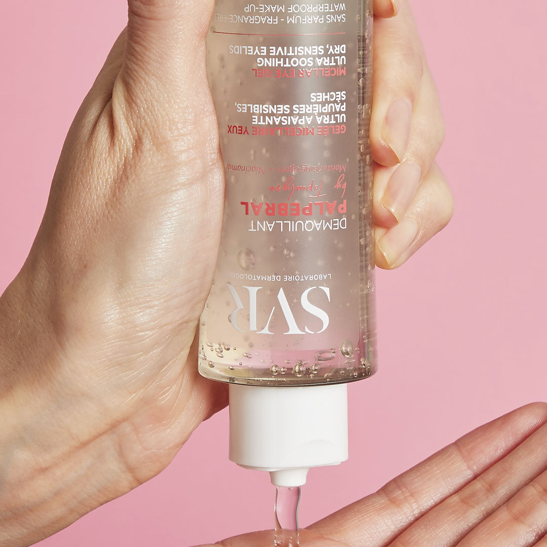 Clear SVR Palpebral micellar eye makeup remover gel being dispensed from a transparent bottle onto a hand against a pink background.