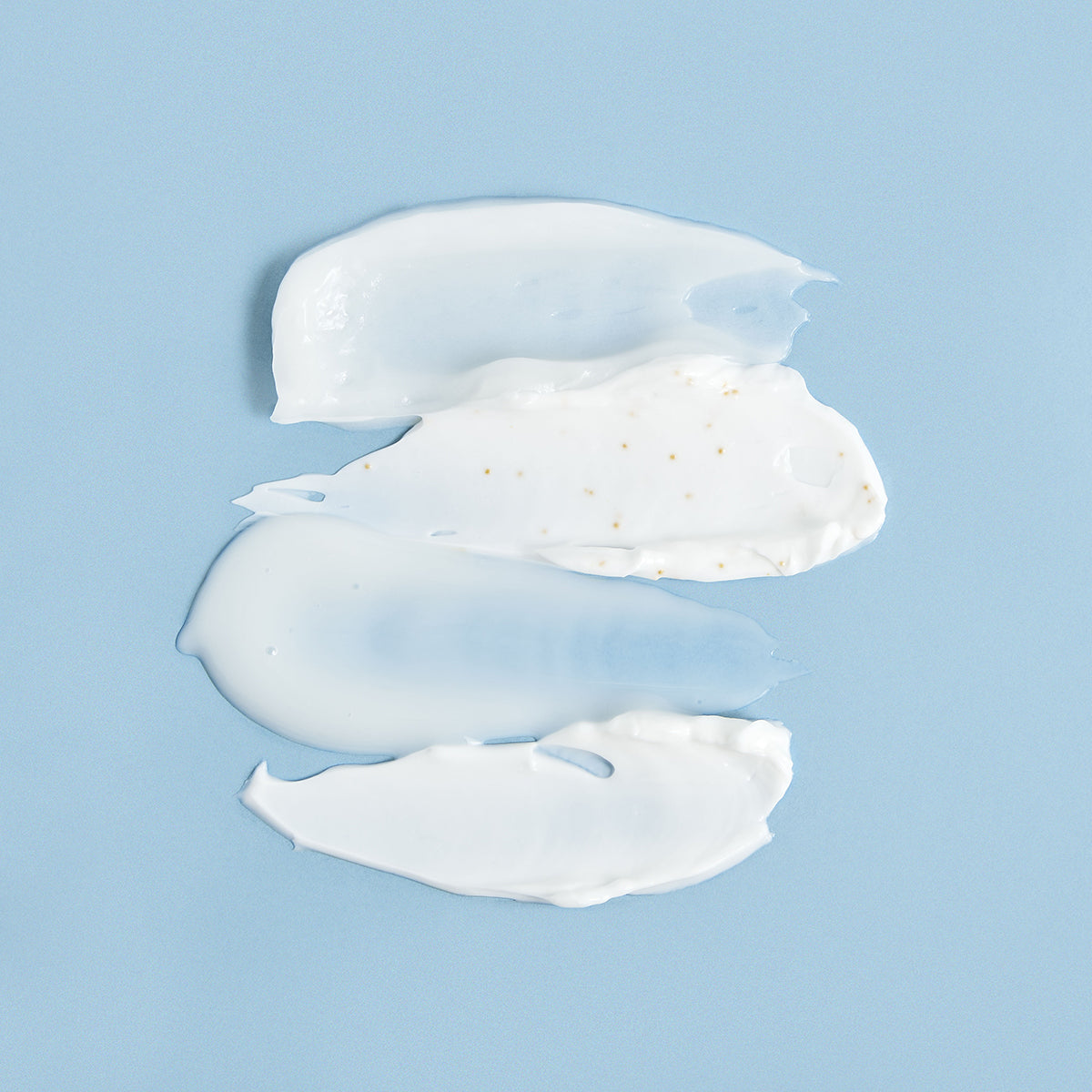 Three smooth, creamy white skincare texture swatches with gold particles layered against a solid light blue background.