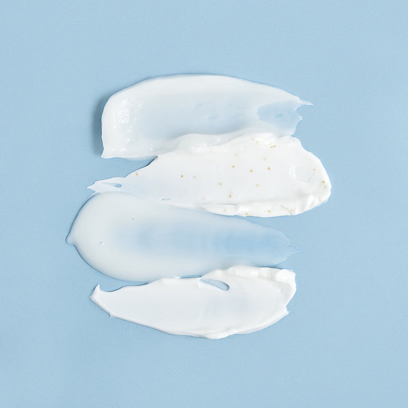 Three smooth, white cream and gel swatches with tiny gold particles layered on a soft blue background.