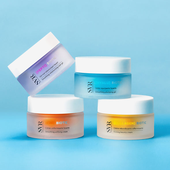 Four SVR Biotic skincare jars in purple, blue, orange, and yellow with white lids arranged on a light blue background.