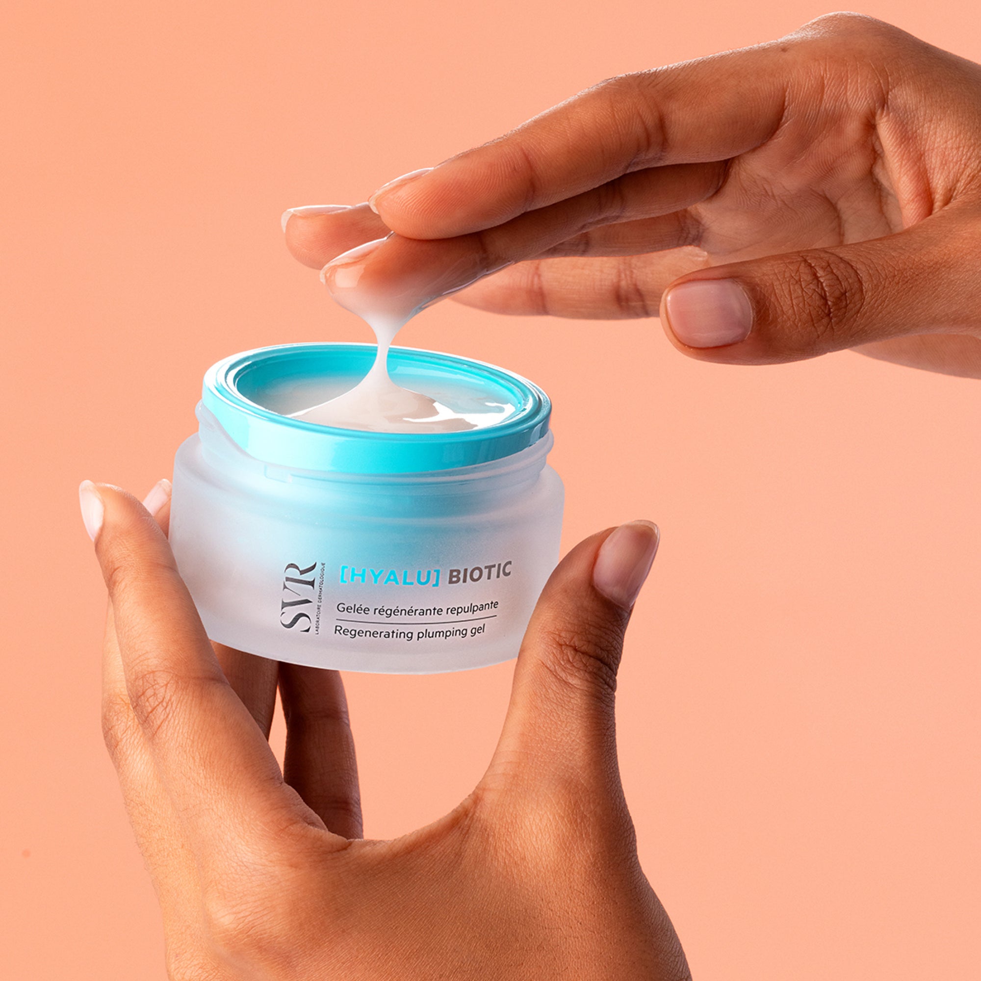 Hands holding a frosted glass jar of SVR HYALU Biotic gel with a bright blue lid and a dollop of white cream.
