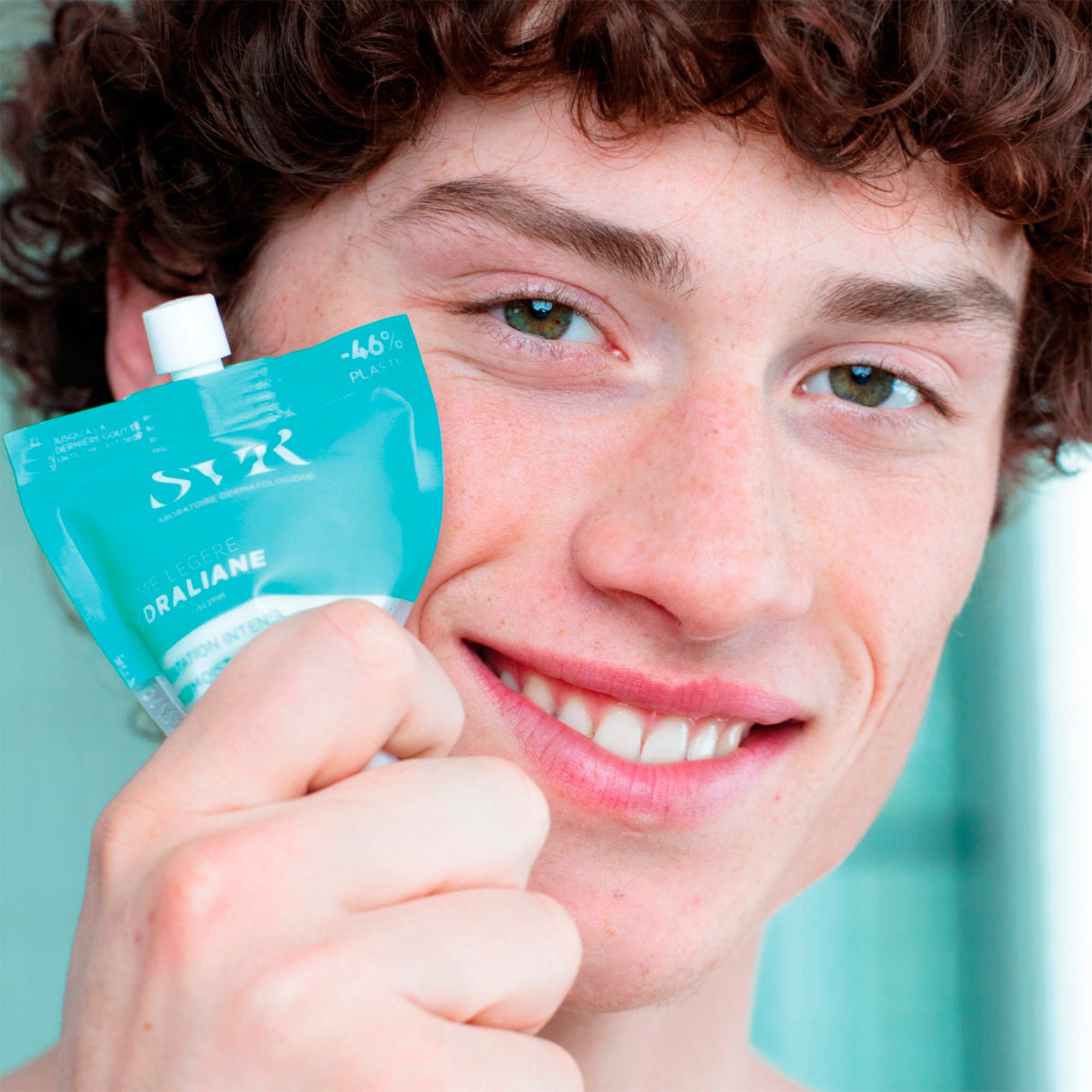 Young man holding turquoise tube of HYDRALIANE Crème Légère hydrating face cream close to his face.