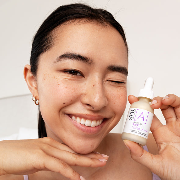 Smiling woman holding a small glass bottle of SVR Ampoule A Lift retinol serum with a white dropper cap.