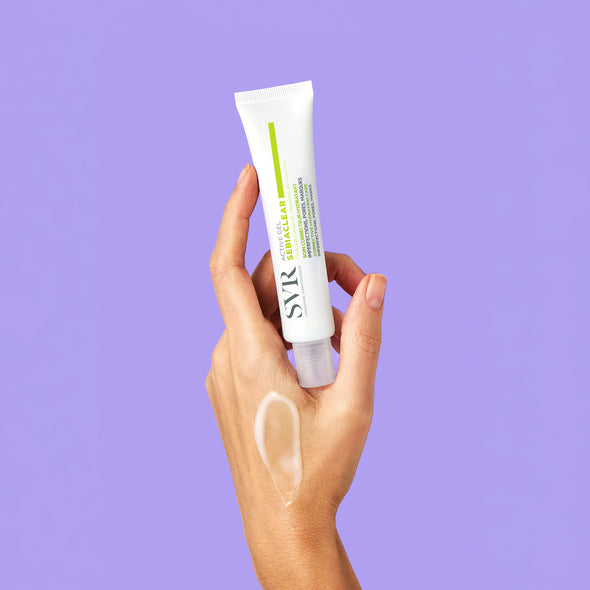 Hand holding a white SVR Sebiaclear Active Gel tube against a purple background with a gel swatch on the skin.