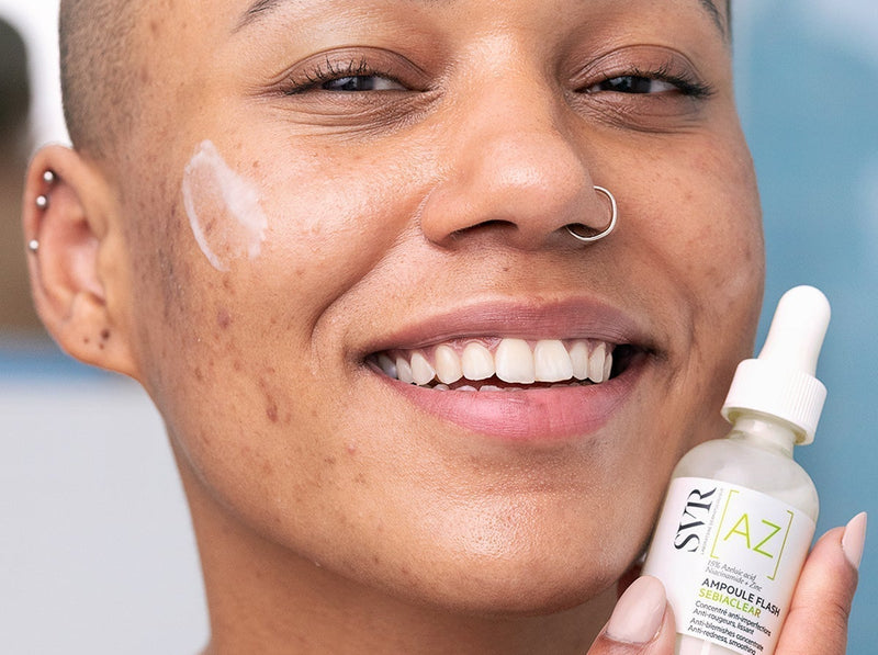 Smiling person with acne-prone skin applying a drop of SVR Sebiaclear serum to their cheek.