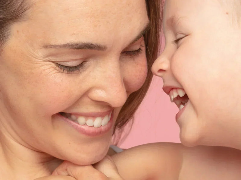 A smiling mother and her young child sharing a tender, affectionate moment against a soft pink background.