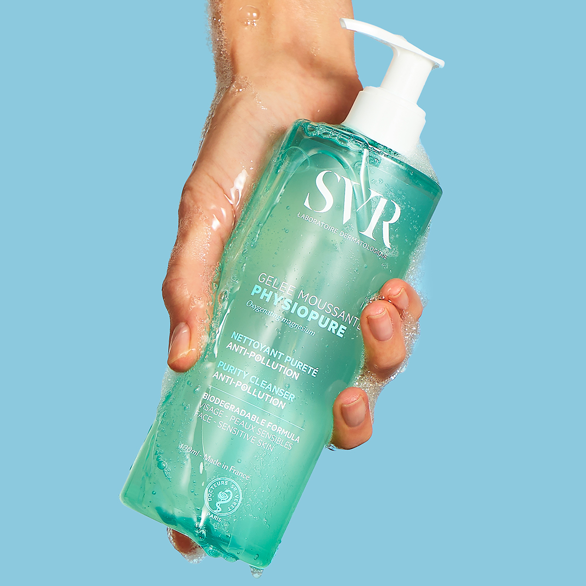 Hand holding a turquoise SVR PHYSIOPURE foaming gel bottle with a white pump dispenser against a light blue background.