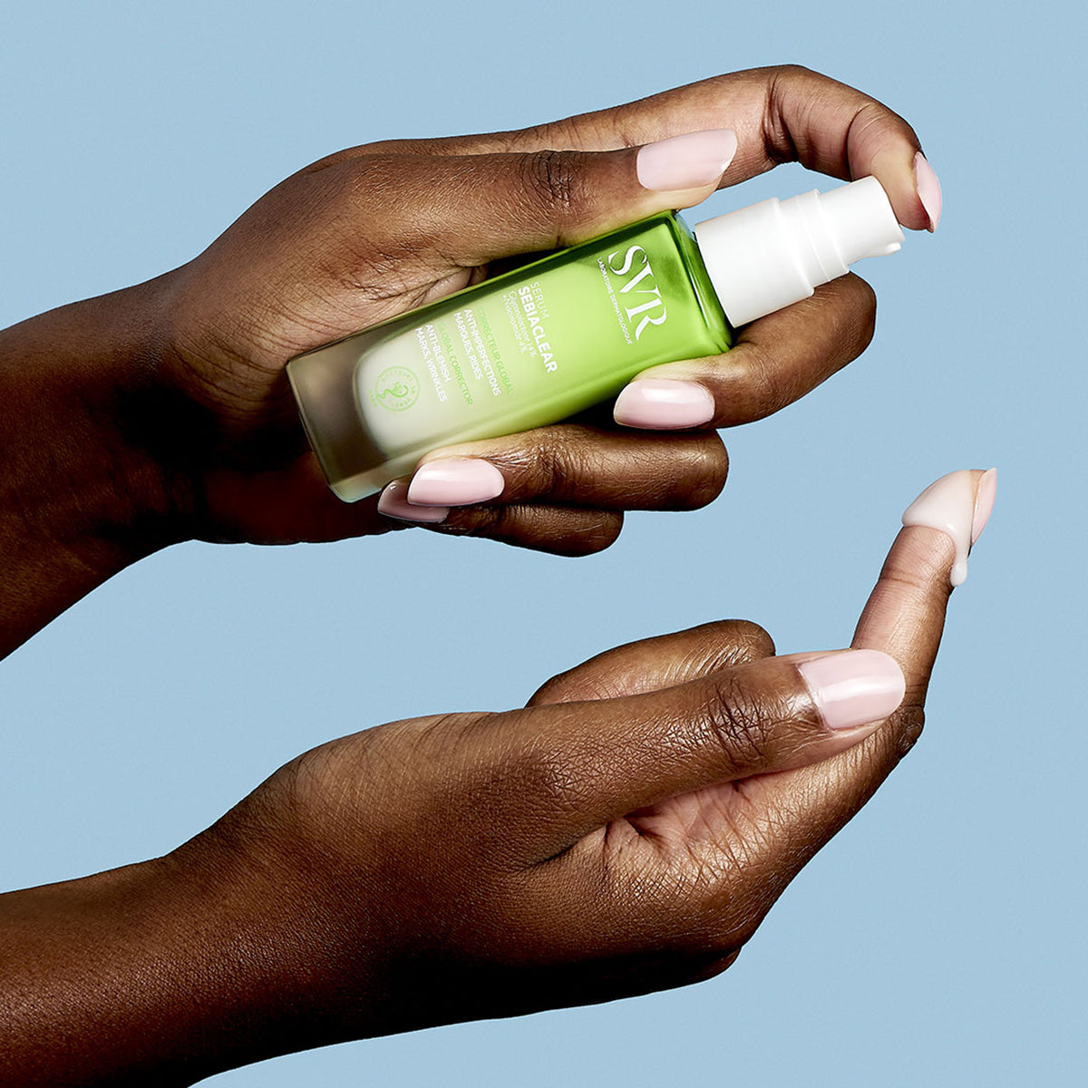 Hands holding a green SVR SEBIACLEAR serum bottle with a white pump, dispensing a drop of cream onto a fingertip.