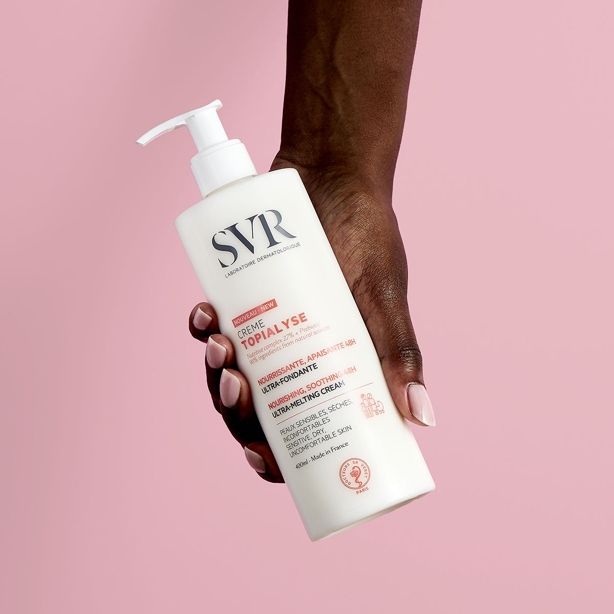 Hand holding a 400ml white SVR TOPIALYSE cream pump bottle against a soft pink background.