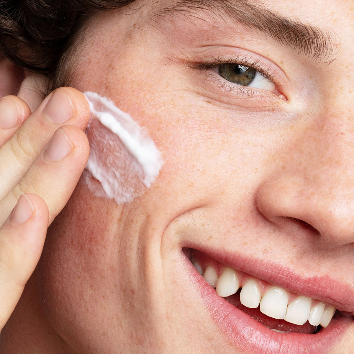 Close-up of a person applying white Hydraliane Light Cream moisturizer to their cheek for 24-hour hydration.