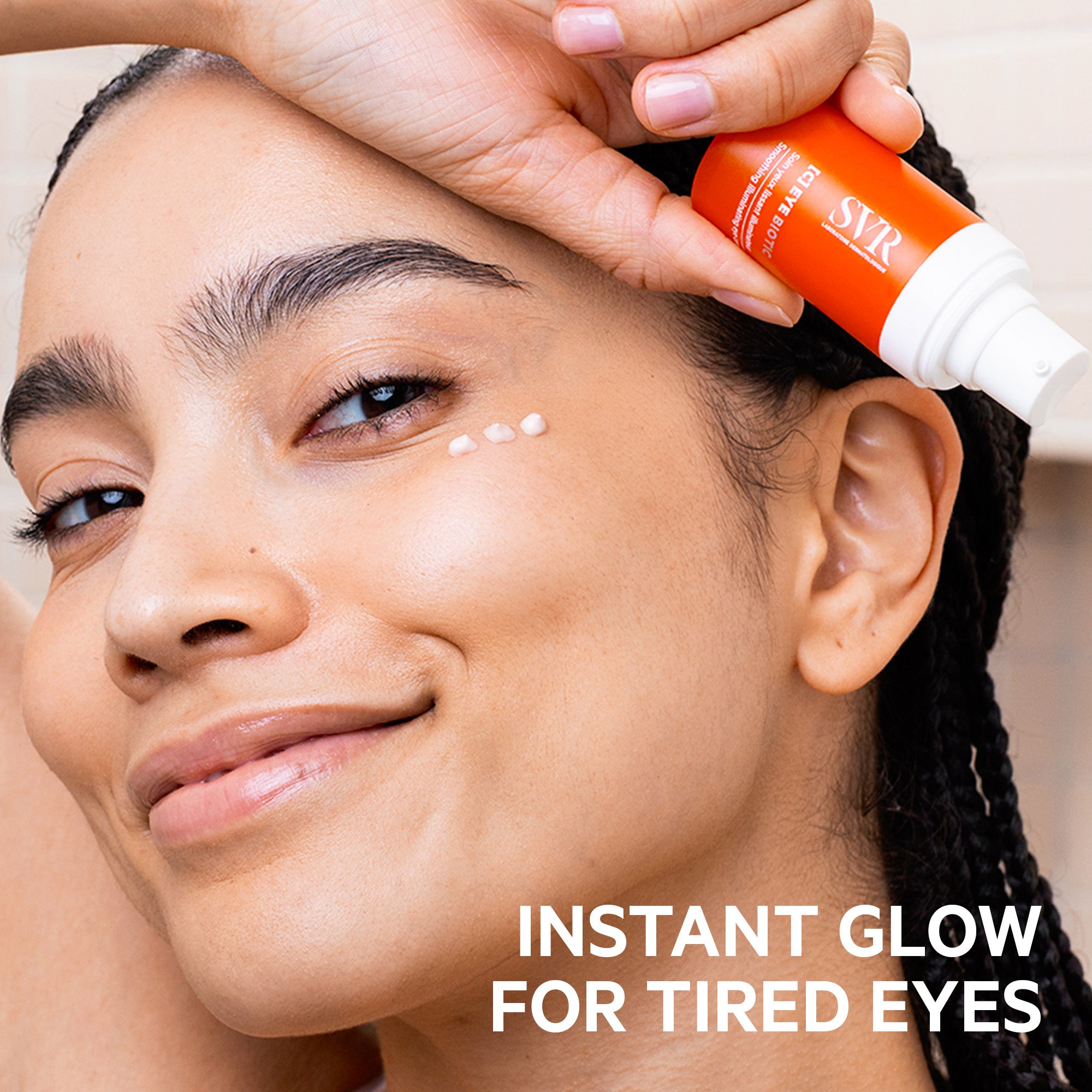 Woman applying SVR [C] Eye Biotic cream from an orange pump bottle onto her under-eye area for a radiant, hydrated look.