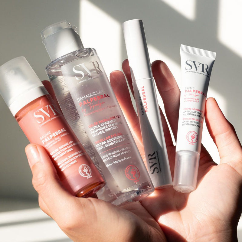 Hand holding four SVR Palpebral skincare products, including eye cream, micellar gel, and mascara, in bright sunlight.