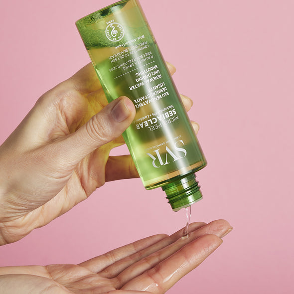 SVR Sebiaclear Micro-Peel green bottle pouring clear liquid into a hand against a soft pink background.