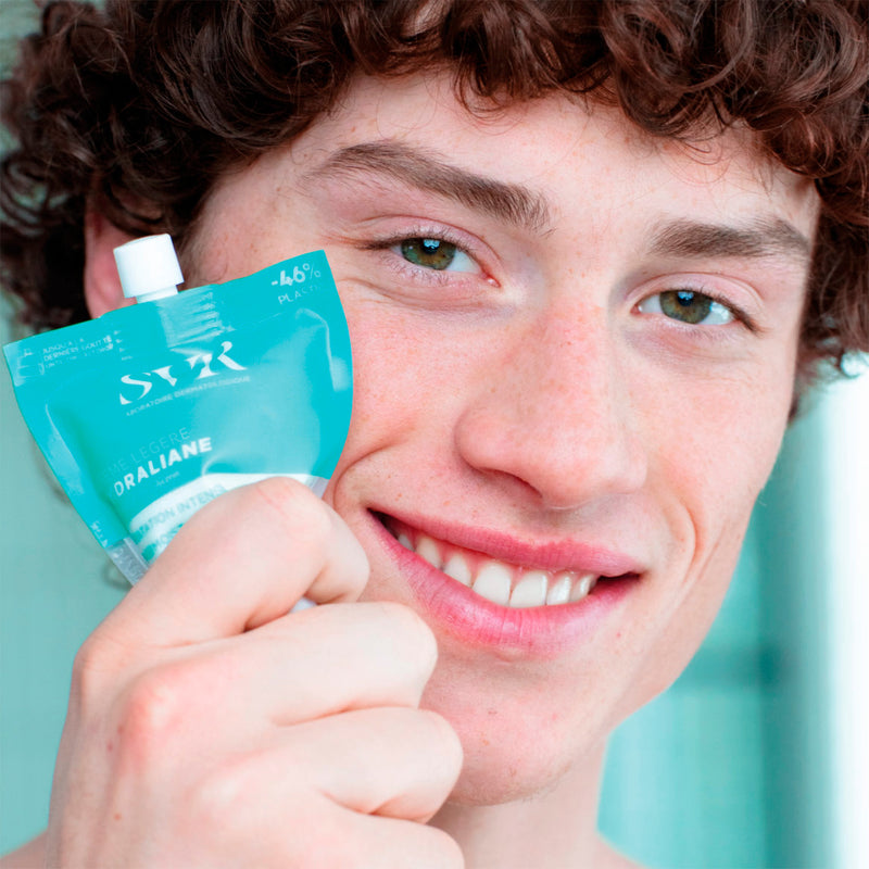 Young man holding turquoise tube of HYDRALIANE Crème Légère hydrating face cream close to his face.