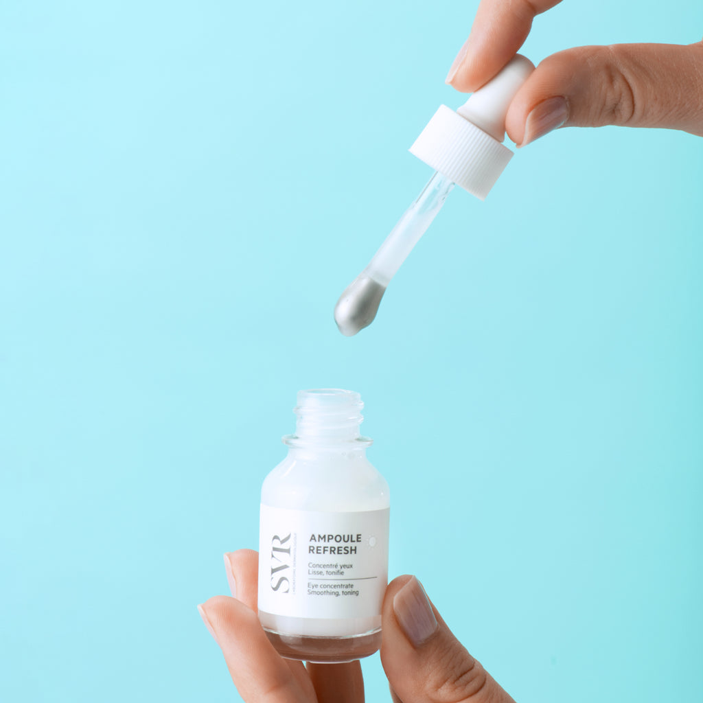 White glass bottle of Refresh Eye Concentrate with dropper dispensing cream against blue background.