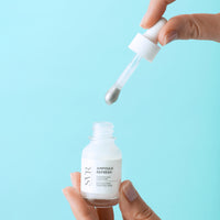 White glass bottle of Refresh Eye Concentrate with dropper dispensing cream against blue background.