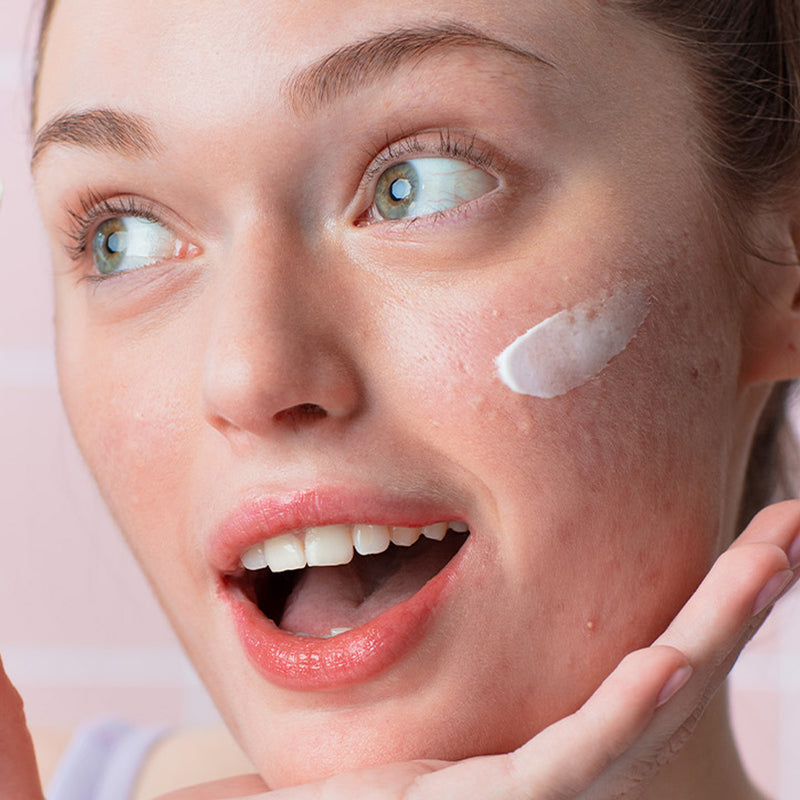 Light cream moisturizer applied on cheek of smiling young woman with clear skin and green eyes.