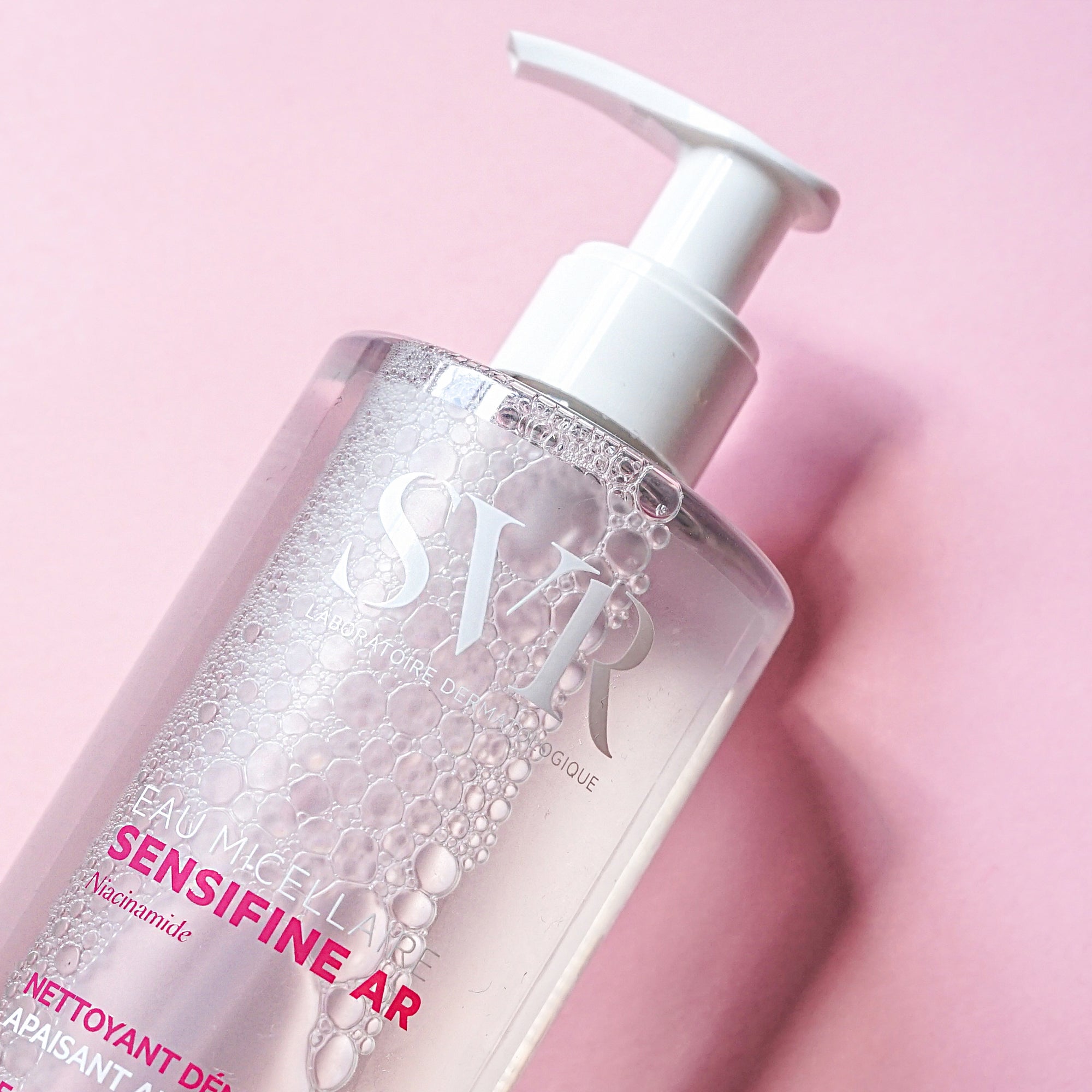 Clear plastic bottle of SVR Sensifine AR Micellar Water with white pump dispenser on pink background.