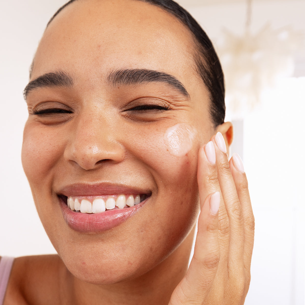 Smiling woman applying clear, fluid SEBIACLEAR serum to her cheek for a smooth, matte finish on acne-prone skin.