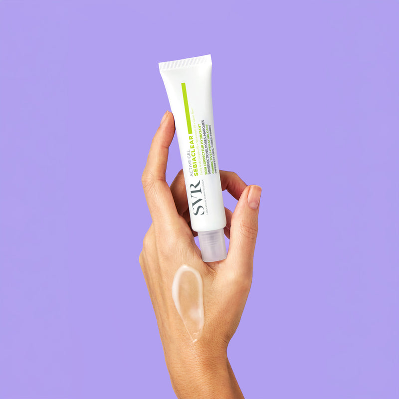 Hand holding a white SVR Sebiaclear Active Gel tube against a purple background with a gel swatch on the skin.